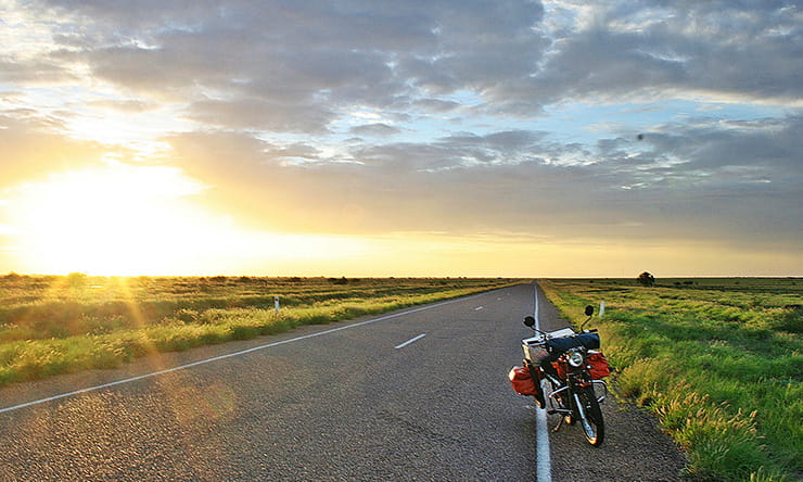 the sunsets while a motorcycle sits at the side of the road